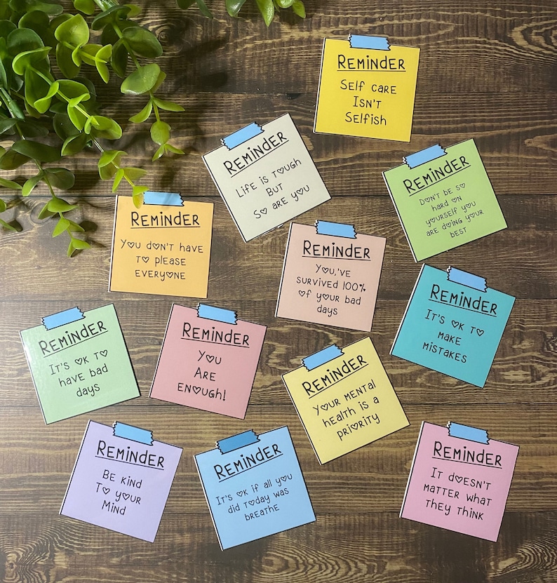 May include: Ten colorful reminder notes with positive messages. The notes are printed with black text and have a white border. The notes are on a wooden surface.