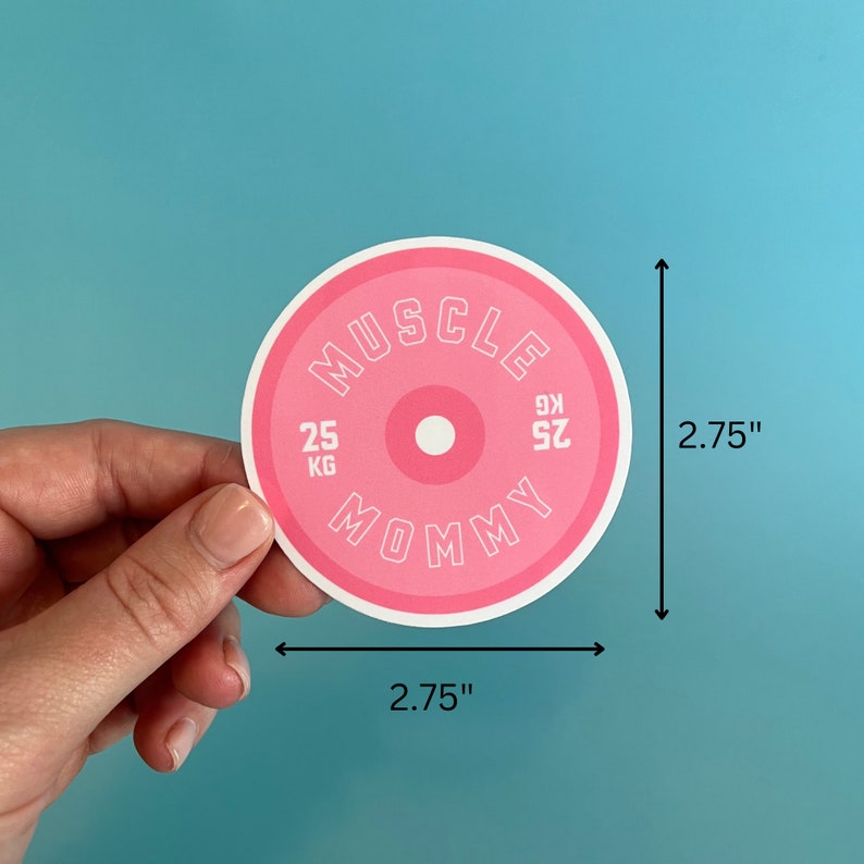 May include: Pink round sticker with the text "MUSCLE MOMMY" in white outlined letters. The sticker is designed to look like a weight plate with the numbers "25 KG" and "25 KG" on either side of a pink circle. The sticker measures 2.75 inches in diameter.