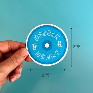 May include: A blue and white round sticker with the text "MUSCLE MOMMY" and "25 KG 52.91" in white. The sticker is 2.75 inches in diameter.