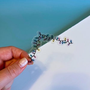 May include: A clear sticker with a string of colorful lights. The lights are outlined in black and have a variety of colors, including pink, blue, yellow, and green.
