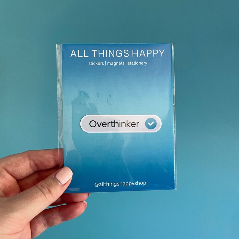 May include: A blue and white sticker with the text "Overthinker" and a checkmark. The sticker is on a blue background with the text "ALL THINGS HAPPY" and "stickers | magnets | stationery" above it. The text "@allthingshappyshop" is at the bottom of the sticker.