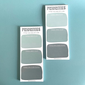 May include: Two rectangular notepads with the word "PRIORITIES" at the top. Each notepad has three sections labeled "THINGS I NEED TO DO", "THINGS I WANT TO DO", and "THINGS FOR OTHER PEOPLE". The background is a light teal color.