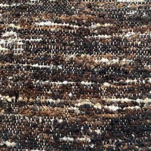 May include: Close-up of a woven rug with a textured surface. The rug has a brown, black, and white color scheme.