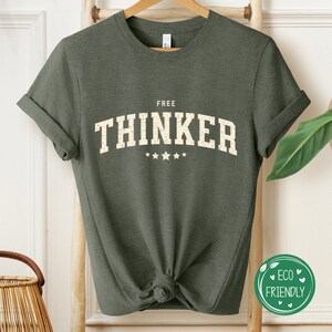 May include: A green t-shirt with the text "FREE THINKER" in white with five white stars underneath. The shirt is made of a soft, comfortable material and has a relaxed fit.