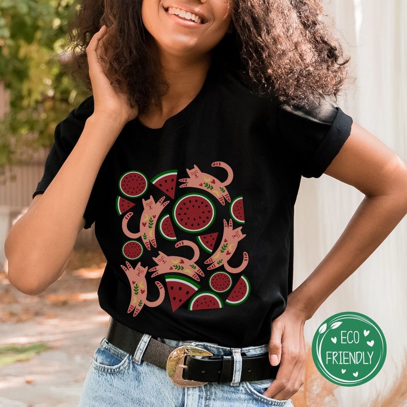 May include: Black t-shirt with a pattern of pink cats and watermelon slices. The cats are stylized and have floral details. The watermelon slices are red with green rinds.