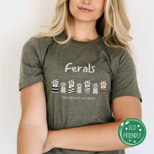 以下が含まれることがあります： 「Ferals」という文字と、「For Childless Cat Ladies」という文字が書かれた、漫画の猫が並んだ緑色のTシャツです。