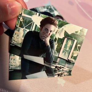 Puede incluir: Una pequeña fotografía rectangular de un hombre con cabello castaño rojizo, vistiendo una camisa oscura de manga larga. La imagen es sostenida por una mano, con otras fotos visibles en el fondo. La foto parece ser un fotograma de una película.