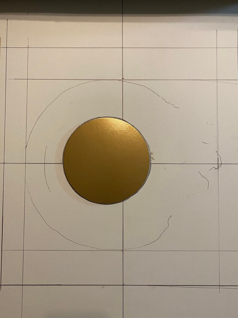 May include: A gold circle is centred on a white surface with a grid pattern. The circle is surrounded by a faint pencil outline of a larger circle.