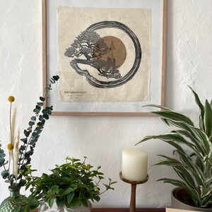 May include: A framed black and white print of a tree with a circle around it. The print is on textured paper and has a brown background. The print is titled "Peppermintcarrot" and is signed by the artist.