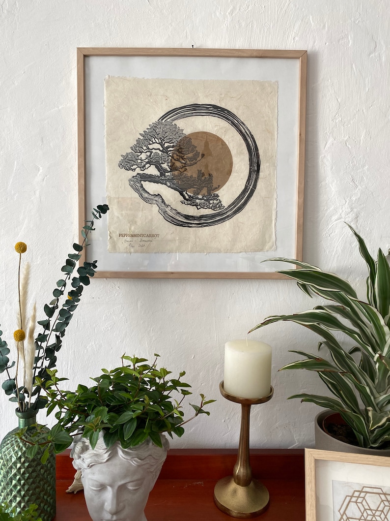 May include: A framed black and white print of a tree with a circle around it. The print is on textured paper and has a brown background. The print is titled "Peppermintcarrot" and is signed by the artist.