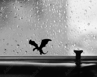 May include: A black silhouette of a dragon sticker on a car window with raindrops.