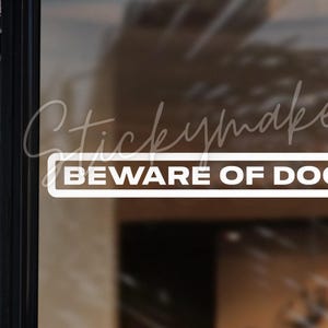 May include: White vinyl sticker with the text "BEWARE OF DOG" in a black rectangle. The sticker is on a glass door.