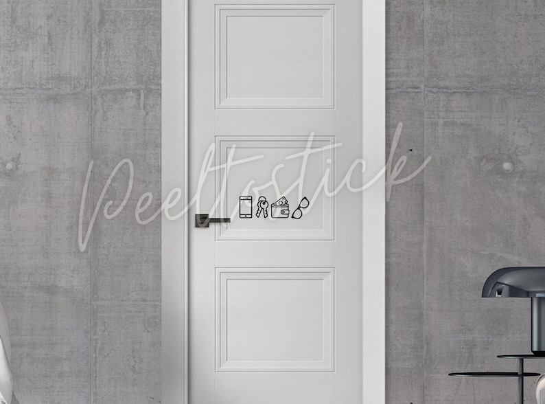 May include: A white door with a black door handle and a black and white sticker of a phone, keys, wallet, and glasses. The sticker is on the middle panel of the door.