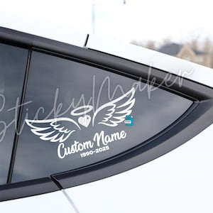 May include: White decal with angel wings, a heart, and a halo, with the text "Custom Name" and dates 1990-2025. The decal is affixed to a car window. The decal is a memorial or remembrance item.