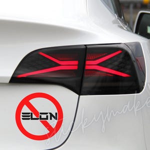 May include: A white car with a red taillight and a red circle sticker with a diagonal line through it and the word "ELON" inside.