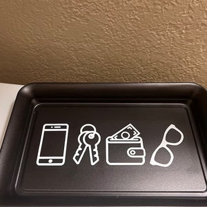 May include: Black tray with white icons of a phone, keys, wallet, and glasses. The tray is designed to hold everyday essentials.