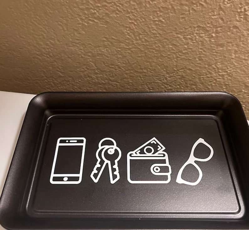 May include: Black tray with white icons of a phone, keys, wallet, and glasses. The tray is designed to hold everyday essentials.