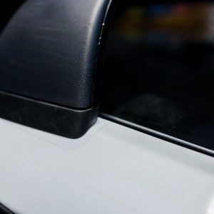 Op de afbeelding: Close-up van een zwarte autodeurgreep met een witte verfchip op de deur.