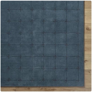 以下が含まれることがあります： 正方形の青いラグで、格子模様があります。 ラグは柔らかい素材でできており、表面は質感があります。 格子線は濃い青色です。 ラグは木の床に置かれています。