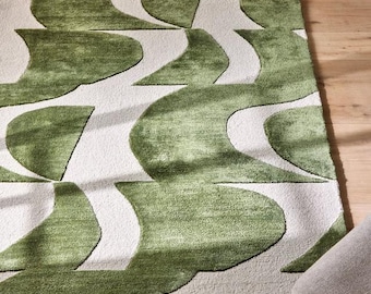 May include: A rectangular area rug with a modern design. The rug features a pattern of green, curved shapes against a white background. The rug is made of a soft, textured material, and is placed on a wooden floor.