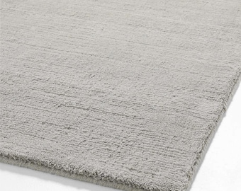 Puede incluir: Una alfombra rectangular gris claro con una superficie texturizada. La alfombra tiene un aspecto suave y afelpado y un color neutro sutil, adecuado para varios estilos de diseño de interiores. Las fibras de la alfombra crean una textura visual.