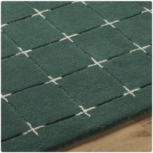 K&ouml;nnte beinhalten: Nahaufnahme eines teal-farbenen Teppichs mit einem Rastermuster aus Quadraten und wei&szlig;en Kreuzdesigns. Der Teppich hat ein weiches, strukturiertes Aussehen, und das Design ist gleichm&auml;&szlig;ig &uuml;ber die Oberfl&auml;che verteilt. Der Teppich ist ein Einrichtungsgegenstand.