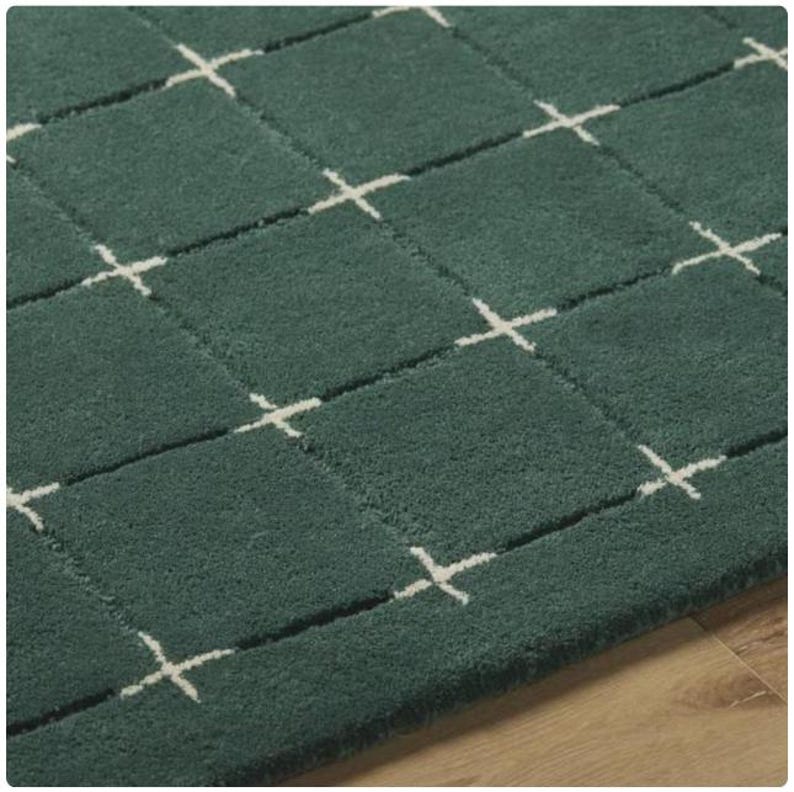 K&ouml;nnte beinhalten: Nahaufnahme eines teal-farbenen Teppichs mit einem Rastermuster aus Quadraten und wei&szlig;en Kreuzdesigns. Der Teppich hat ein weiches, strukturiertes Aussehen, und das Design ist gleichm&auml;&szlig;ig &uuml;ber die Oberfl&auml;che verteilt. Der Teppich ist ein Einrichtungsgegenstand.