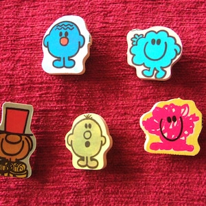 May include: Five small, colourful, cartoon character figurines with different facial expressions. The characters are Mr. Happy, Mr. Grumpy, Mr. Messy, Mr. Nervous, and Mr. Gloomy.