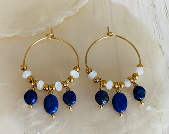 May include: Gold hoop earrings with white and blue gemstone beads. The earrings have a dangling design with three blue oval-shaped beads hanging from each hoop.