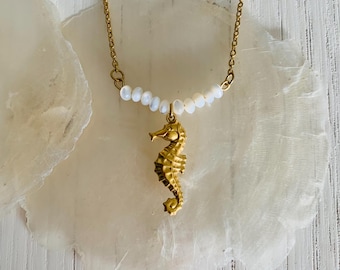 May include: A gold chain necklace with a gold seahorse charm and a row of white pearl beads.