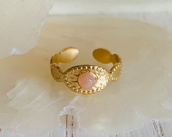 May include: Gold ring with a pink oval gemstone set in a textured band.