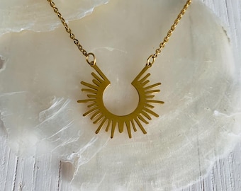 May include: A gold necklace with a sunburst pendant. The pendant is a circle with rays emanating from it.