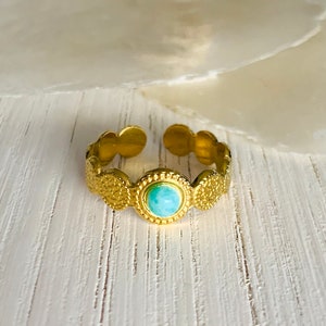 Puede incluir: Un anillo de oro con una piedra turquesa engastada en el centro. El anillo está decorado con un diseño texturizado.