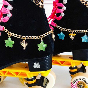 May include: Black roller skates with gold chains and star and cartoon character charms. The wheels are yellow and have a black and white striped design. The text "Street Flow" is printed on the wheels.