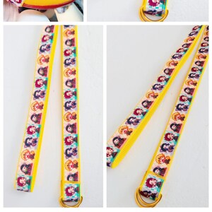 May include: Two yellow straps with a repeating pattern of colourful anime characters. The straps have a gold metal ring at one end.