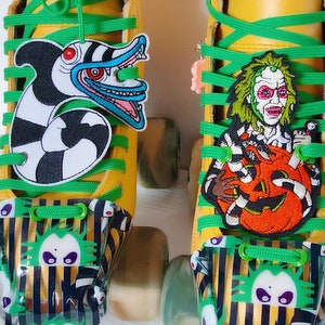 May include: A pair of yellow roller skates with green laces and black and white striped toe stops. The skates have patches on them, one with a character from the movie Beetlejuice and the other with a character from the movie The Nightmare Before Christmas.