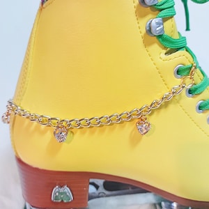 May include: Yellow roller skate with a green lace and a gold chain with heart-shaped charms with clear rhinestones.