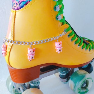 May include: Yellow roller skates with green laces and a chain with pink cat charms. The wheels are clear with green and white swirls. The wheels have the word "Mellows" printed on them.
