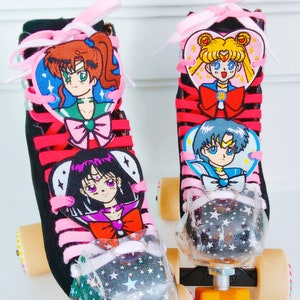 May include: Pair of black roller skates with pink laces and cartoon character patches. The skates have clear toe stops filled with glitter and star accents. The wheels are beige and the trucks are orange.
