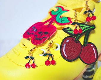 Peut inclure: Patins à roulettes jaunes avec des patchs de cerises rouges et vertes et de crânes. Le patin a des breloques de cerises dorées accrochées aux lacets.