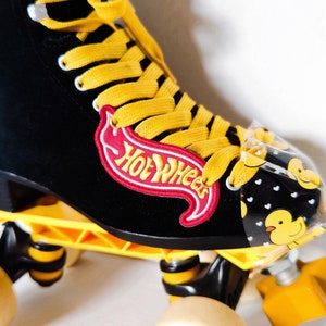May include: Black roller skates with yellow wheels and laces. The skates have a Hot Wheels logo on the side and a clear plastic cover with a duck pattern.