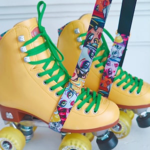 May include: A pair of yellow roller skates with green laces and colourful patterned straps. The skates have clear wheels and black trucks.