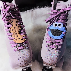 May include: A pair of purple roller skates with sparkly glitter on the sides. One skate has a cookie monster patch and the other has a cookie patch.