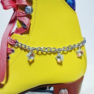 May include: Yellow roller skate with red laces and a silver chain with star-shaped charms. The skate has brown wheels and a brown base.