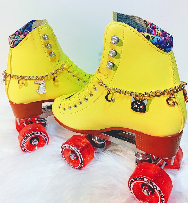 Peut inclure: Patins &agrave; roulettes jaunes avec des breloques de personnages noirs et blancs sur les lacets. Les roues sont rouges avec des lettres noires. Les patins ont un motif color&eacute; &agrave; l'int&eacute;rieur de la botte.