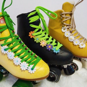 May include: Three roller skates in yellow, black, and mustard yellow. The yellow and black skates have green laces, while the mustard yellow skates have tan laces. All three pairs of skates are decorated with daisy and flower accents.
