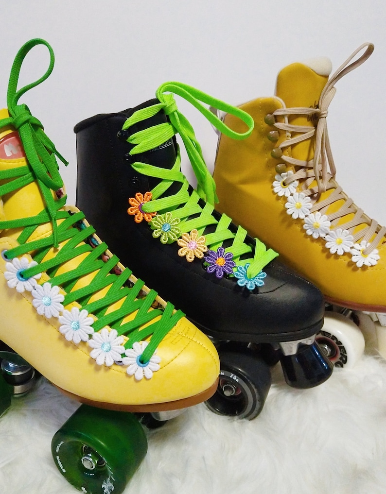 May include: Three roller skates in yellow, black, and mustard yellow. The yellow and black skates have green laces, while the mustard yellow skates have tan laces. All three pairs of skates are decorated with daisy and flower accents.