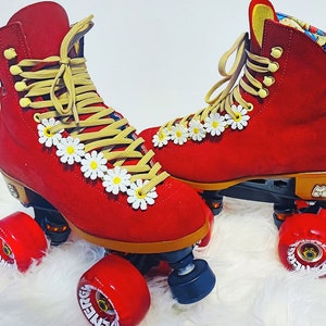May include: A pair of red roller skates with daisy accents. The skates have tan laces and red wheels. The boots are a vibrant red with white daisy embellishments along the laces. The wheels are red and the base is black.
