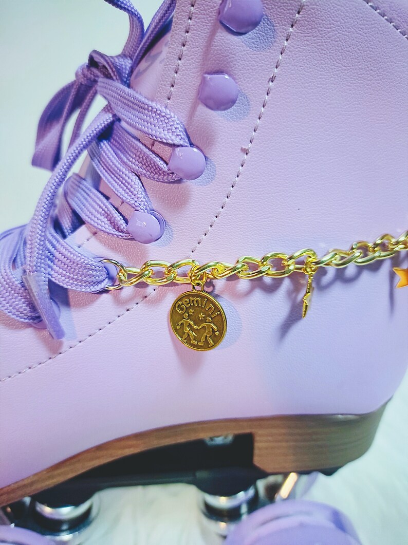 May include: Purple roller skates with a gold chain and a gold charm that says "Gemini" with a symbol of two people holding hands.
