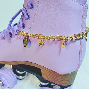 May include: Purple roller skate with a gold chain and star charms around the ankle. The skate has a wooden base and purple wheels.